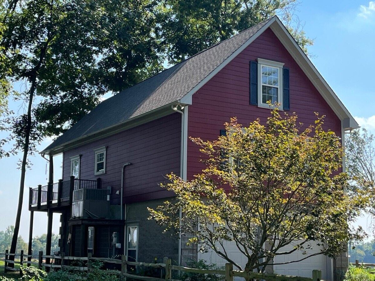 Side view of a remodeled garage with a red exterior and new roofing in a wooded area by Wolfe Construction in Jackson, TN