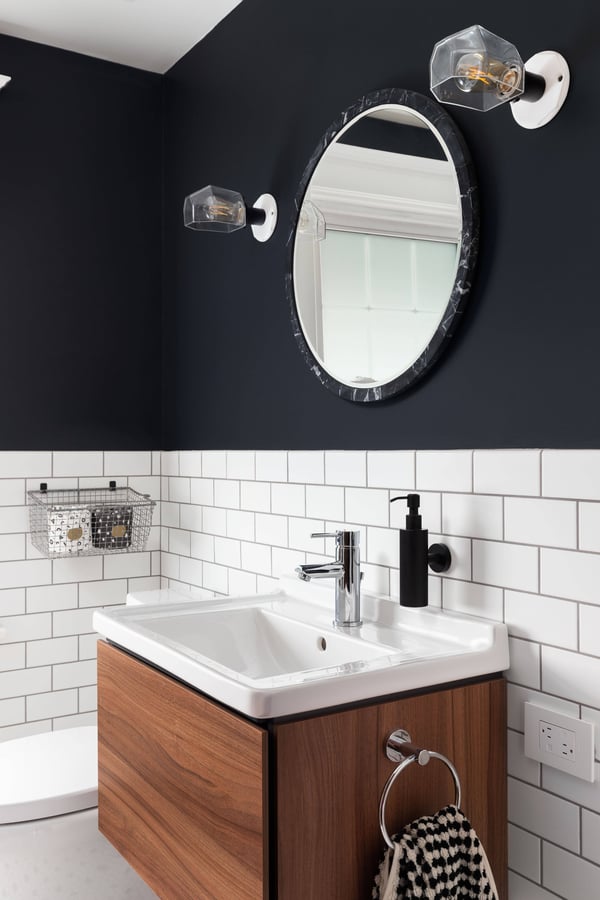 West Tennessee-Remodeling Company- Wolfe Construction Co.-A bathroom sink detail with dark blue walls, subway tiles, a circular mirror, and a floating wood cabinet West Tennessee-Remodeling Company- Wolfe Construction Co.-A bathroom sink detail with dark blue walls, subway tiles, a circular mirror, and a floating wood cabinet