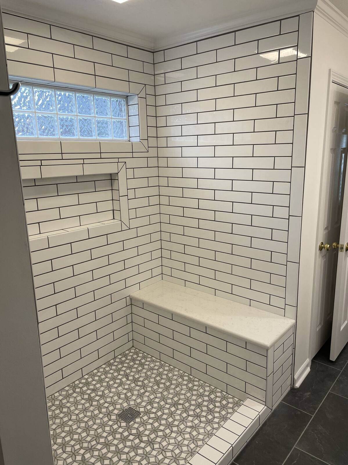 Custom white subway tile shower with built-in bench seating and decorative floor tiles by Wolfe Construction in Jackson, TN