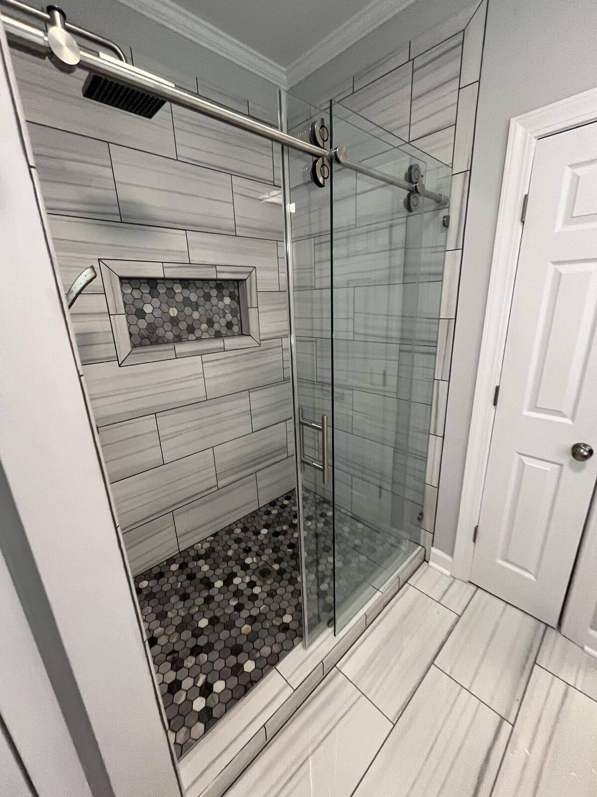 Frameless glass shower with hexagonal tile flooring and modern wall tile by Wolfe Construction in Jackson, TN