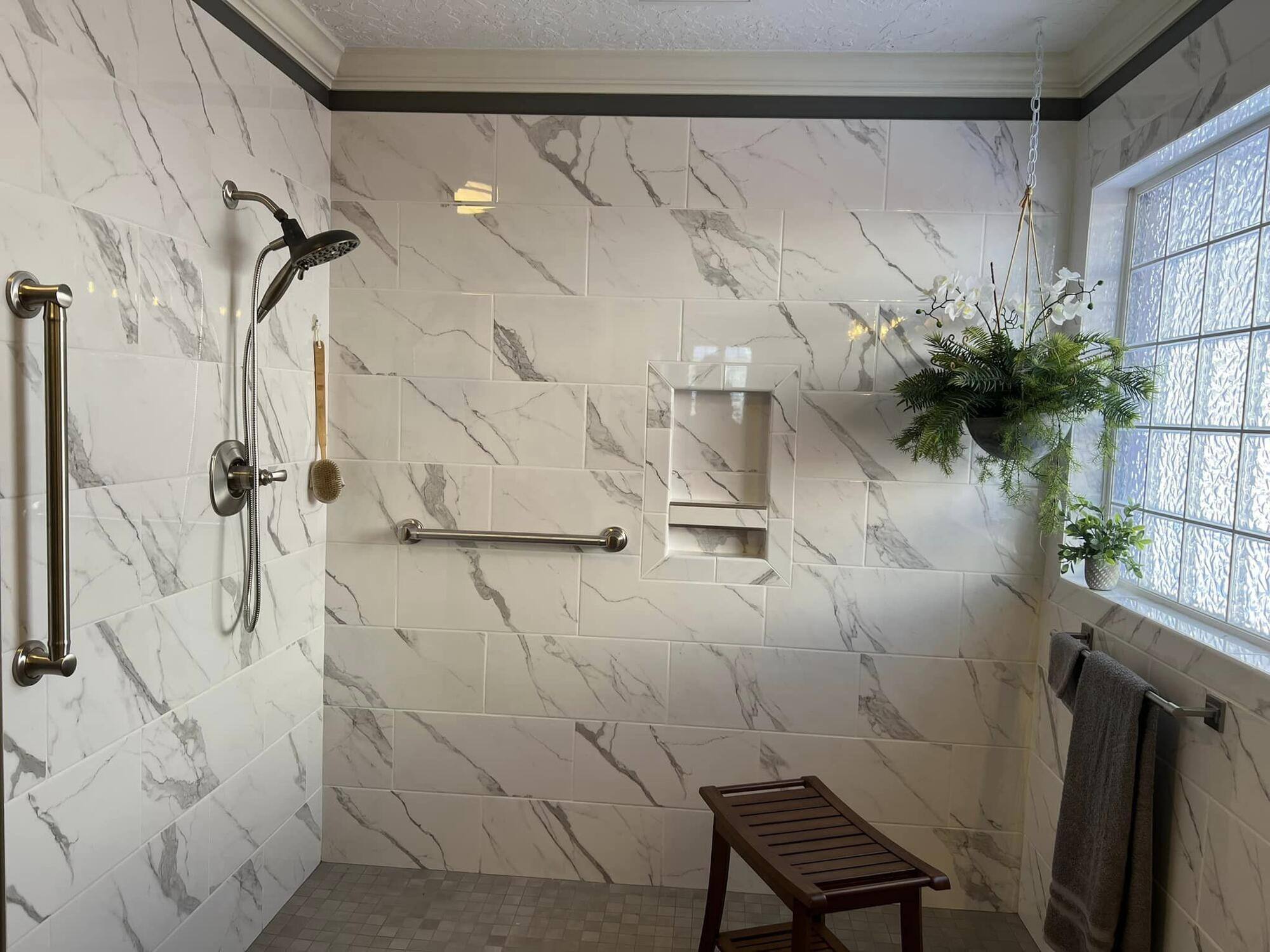 Spacious marble-tiled shower with grab bars and built-in shelving by Wolfe Construction in Jackson, TN